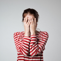 woman wearing a red and white striped shirt covering her face with her hands