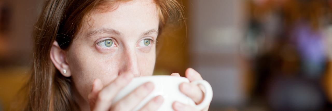 A woman drinking out of a coffee mug.