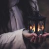 close up of woman holding tea light candle in in small lantern with both hands