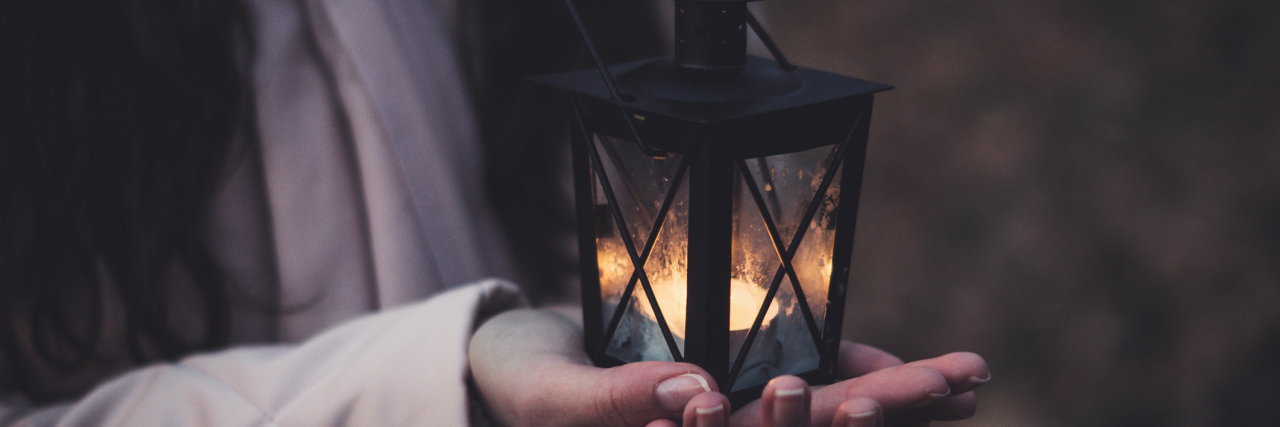 Why I Always Light a Candle on Nights I Struggle With Depression close up of woman holding tea light candle in in small lantern with both hands