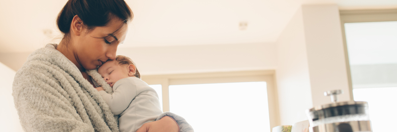 What a Day Is Like for a Mother With Chronic Illness mother wearing a robe and holding her baby son in her arms