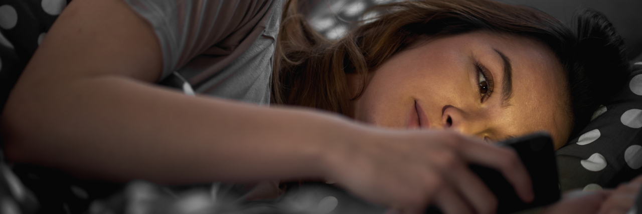 young woman lying in bed on phone