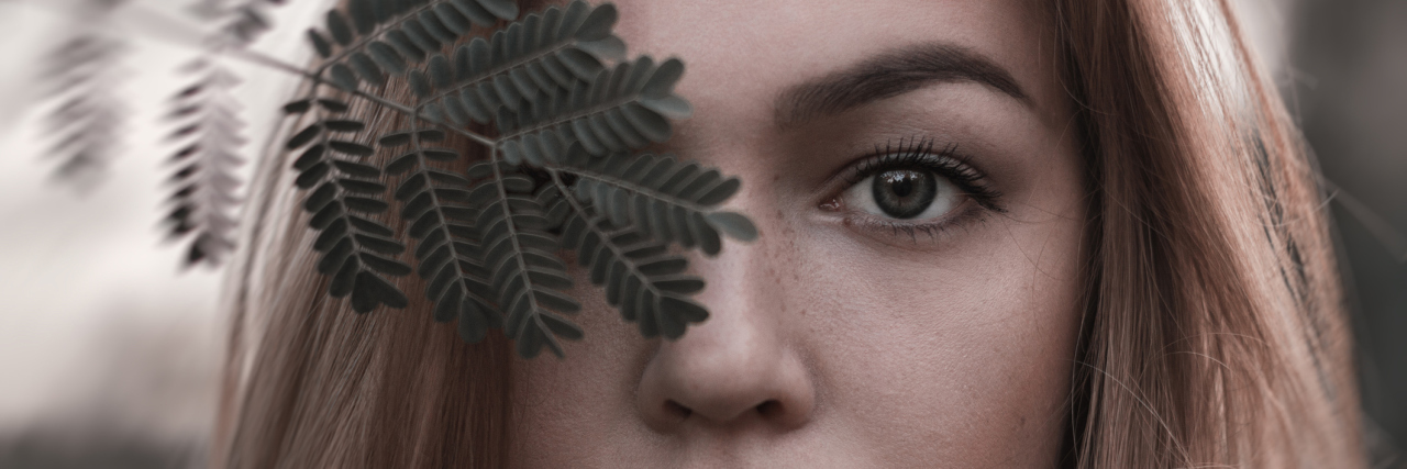 ME/CFS: What a Person With Invisible Illness Feels and Experiences woman with blonde hair and green eyes standing outside with a leaf covering one of her eyes