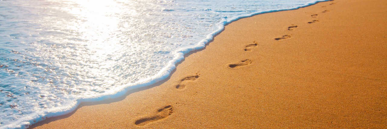 Beach, wave and footprints at sunset.