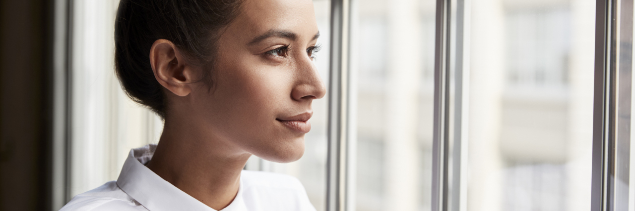 woman with a white shirt and a bun looking out the window