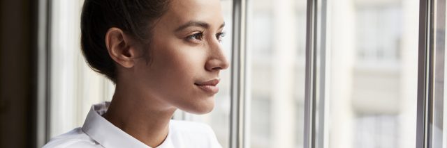 woman with a white shirt and a bun looking out the window