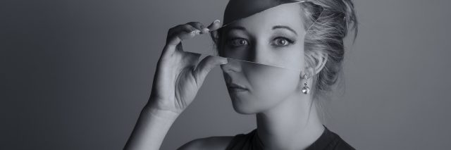 double exposure black and white photo of woman holding shard of mirror up to face covering eyes with different reflection