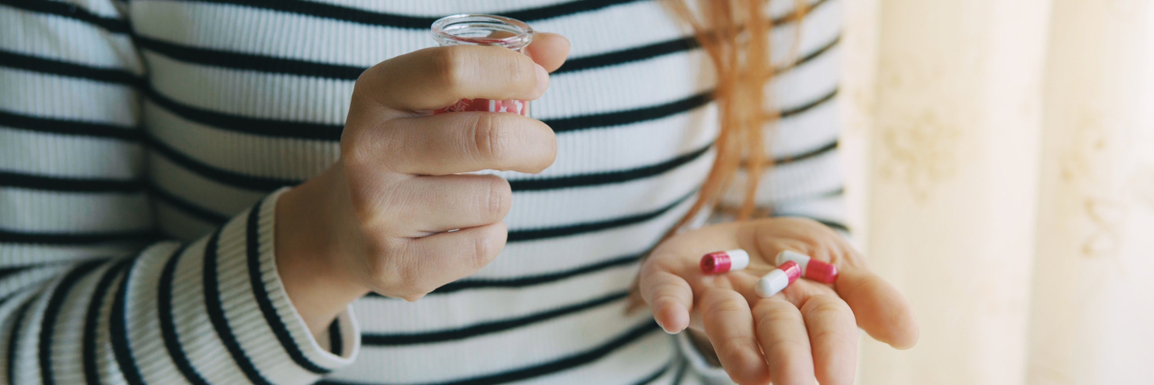 Dear Anti-Anxiety Medication: I’m Sorry I Struggled to Accept You young redhead woman holding pills in hand and cup