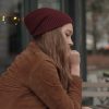 woman wearing a brown jacket and red beanie sitting outside at a cafe by herself