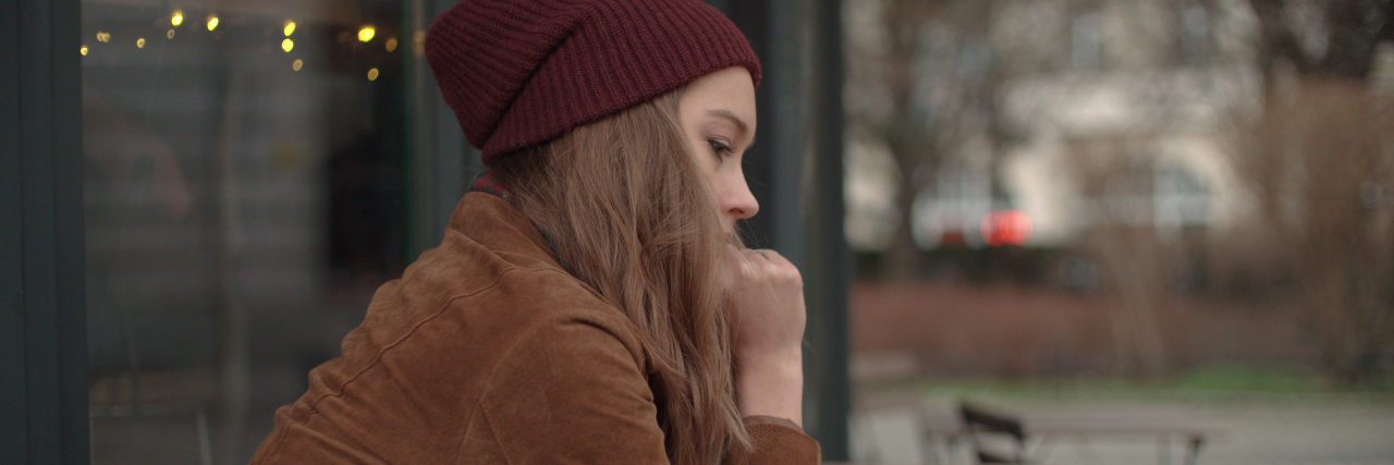 woman wearing a brown jacket and red beanie sitting outside at a cafe by herself