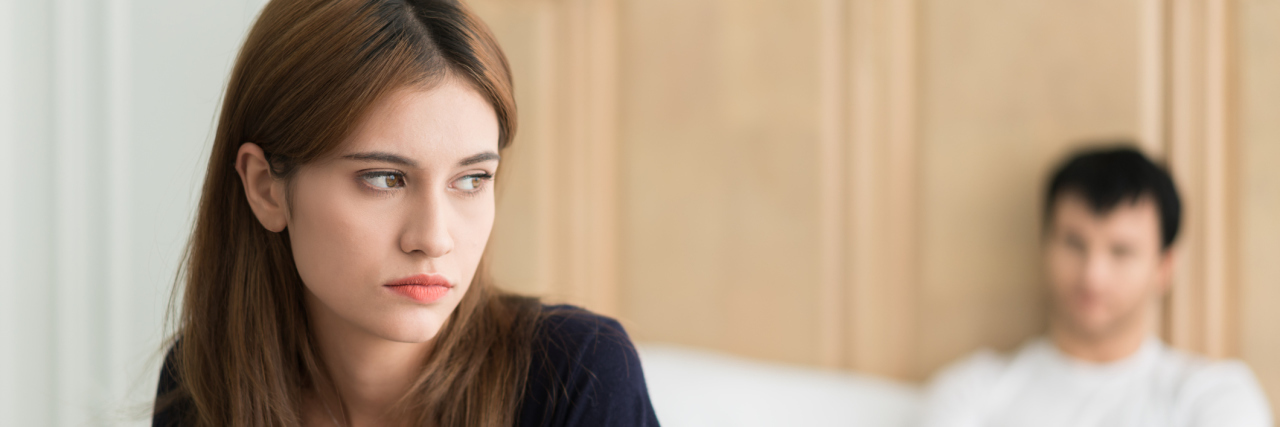 Struggling With Endometriosis and Painful Sex man sitting up in bed with his arms crossed and a woman sitting on the edge of the bed sadly looking away