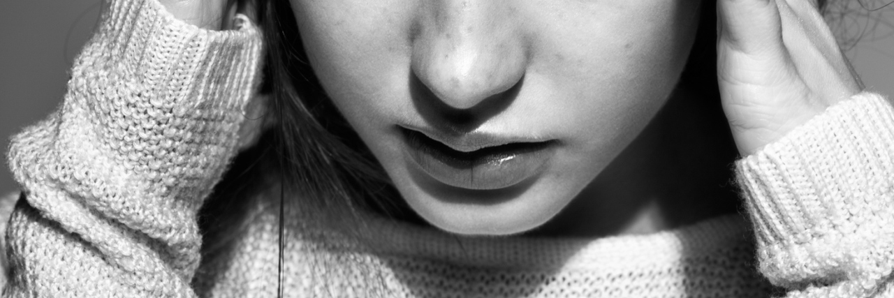 Questions People Who Struggle With Self-Harm Don’t Want to Be Asked young woman in white pullover sweater against gray background looking depressed or upset