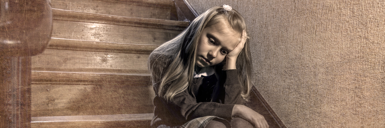 7 or 8 years old sad depressed and worried schoolgirl sitting on staircase desperate and scared suffering bullying and harassment at school in dramatic lighting and bullied children grunge edit