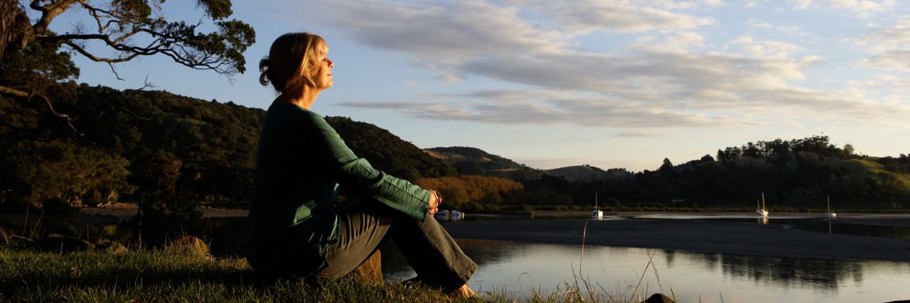 Slowing Down When You Live With Chronic Illness woman sitting by the lake at sunset enjoying the quiet