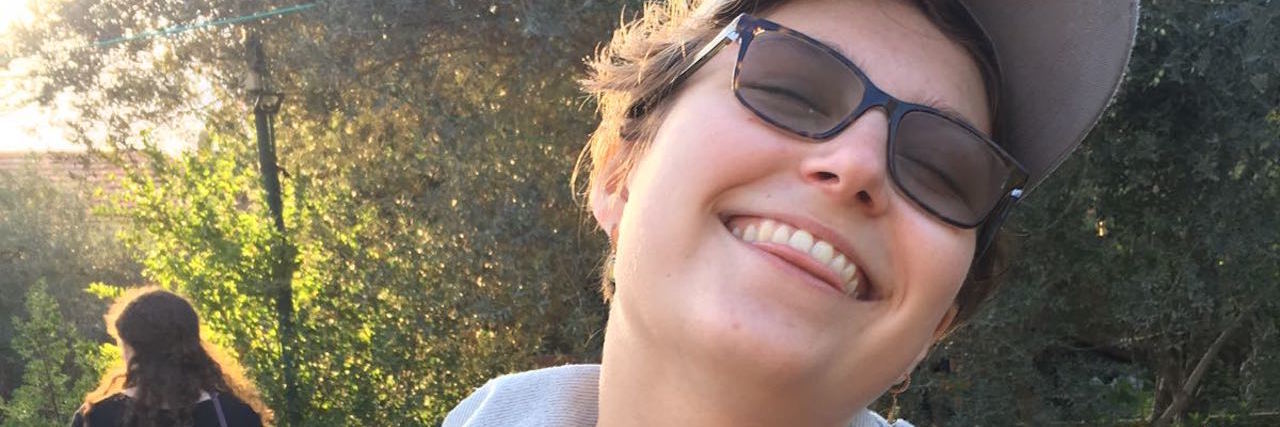 How Chronic Pain Is Like an Invisible Friend woman standing outside smiling wearing a hat and sunglasses