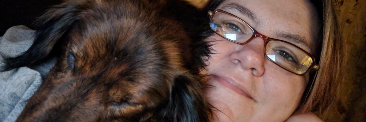 What a Day With Chronic and Mental Illness Is Like woman lying on a couch with her weiner dog on her shoulder