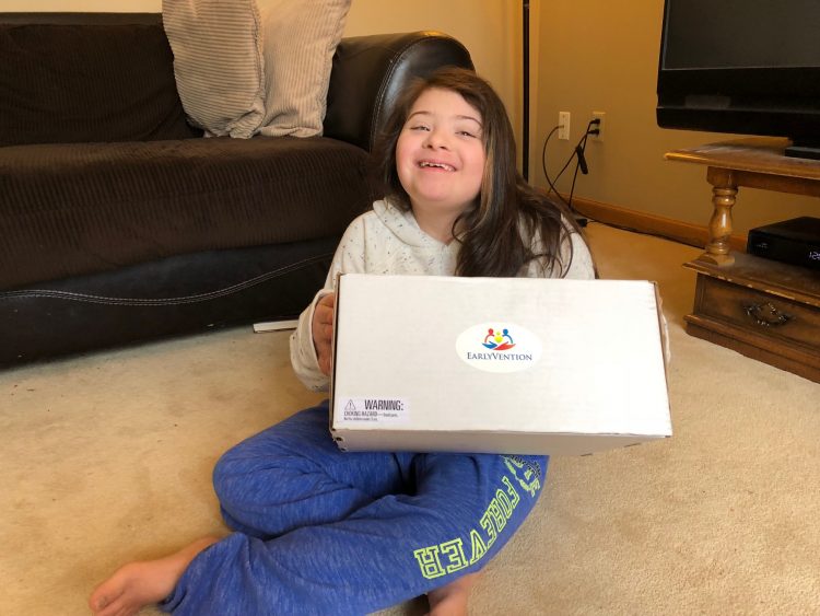 Girl with Down syndrome holding an EarlyVention box smiling