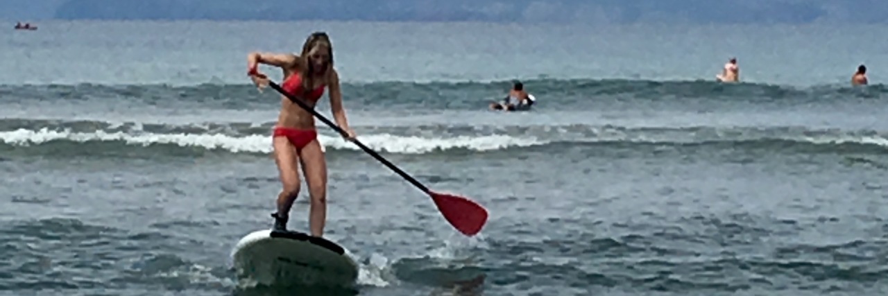 Embracing Your Health Struggles and Embarrassing Moments woman paddleboarding through waves in the ocean