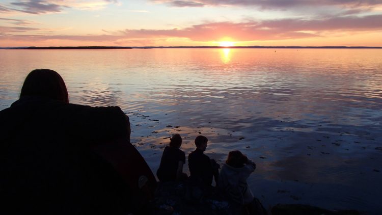 silhouette of friends sitting on a beach looking at the sunset over the ocean