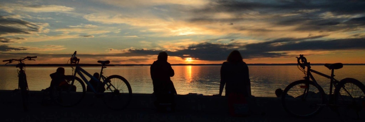 Having Supportive Friends in College to Help You With Chronic Pain silhouette of friends and their bikes sitting on the beach watching a sunset over the ocean