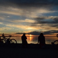 silhouette of friends and their bikes sitting on the beach watching a sunset over the ocean