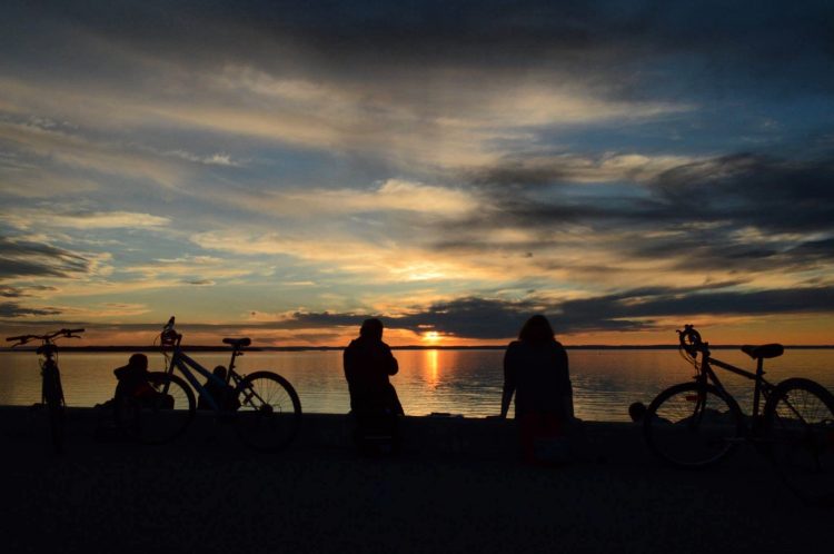 silhouette of friends and their bikes sitting on the beach watching a sunset over the ocean