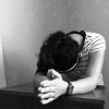black and white photo of woman leaning on desk praying