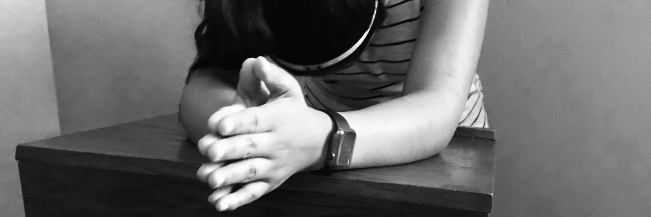 What a Bipolar Disorder Hallucination Looks Like black and white photo of woman leaning on desk praying