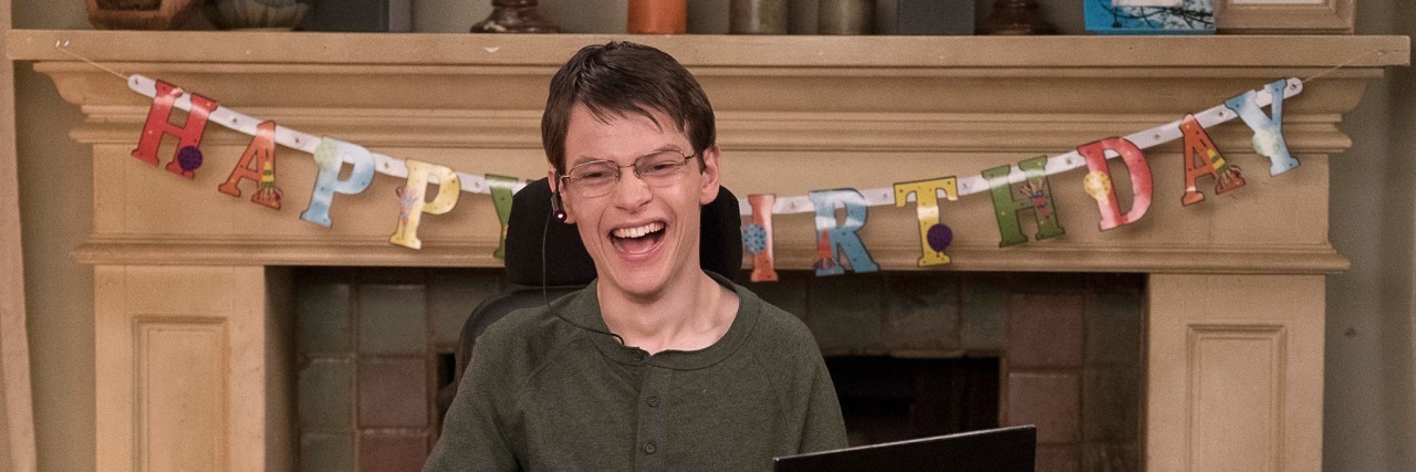 Speechless' Birthday Episode Challenged How I Parent My Disabled Child JJ smiling at camera, "Happy Birthday" banner in the background draped across the mantel.