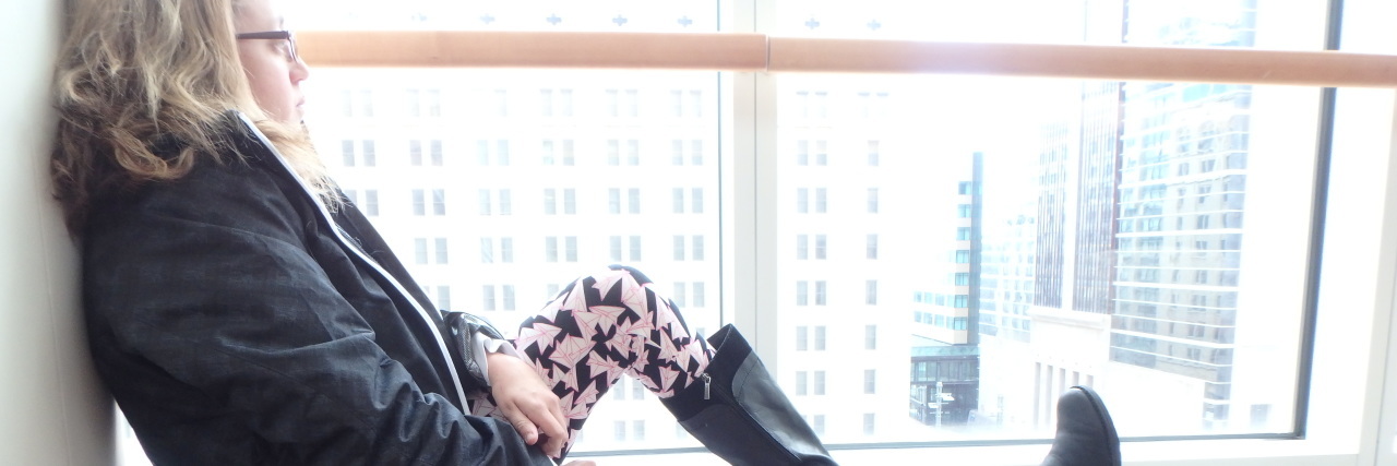 When You Have to Give Up a Dream Due to Chronic Illness woman in a black coat, rainboots and pink leggings sitting on a window ledge