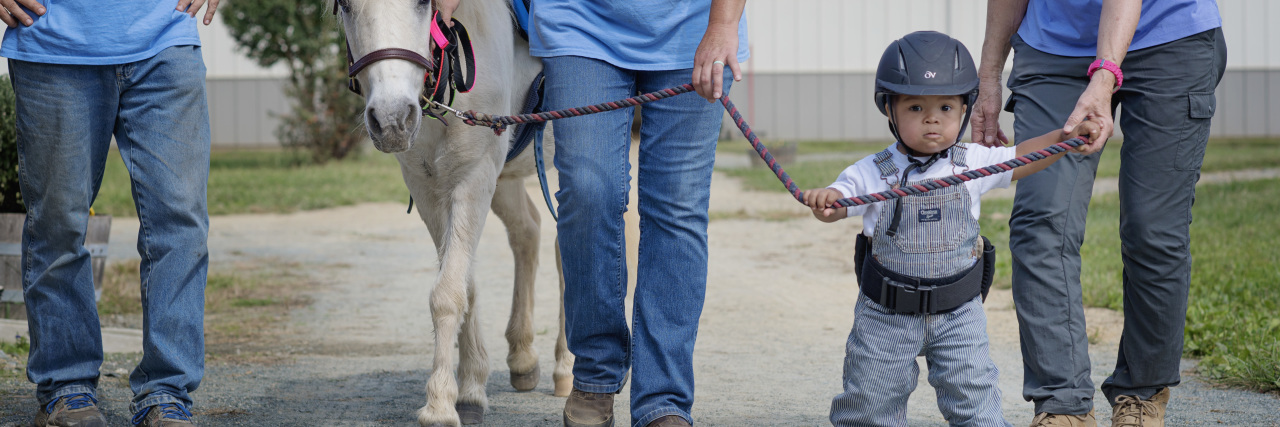 The Woman I've Become Because of My Child With Down Syndrome Adorable toddler with Down syndrome "walking" horse with two adults.