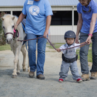 Adorable toddler with Down syndrome "walking" horse with two adults.