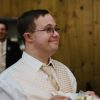 Young man with Down syndrome dressed up at wedding holding plate with slice of cake