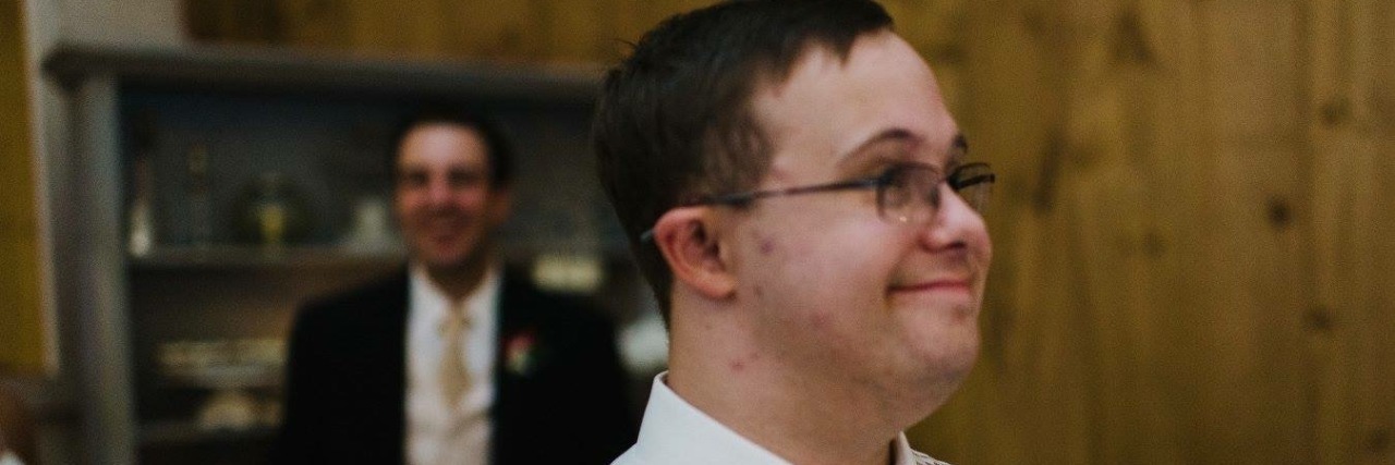 On Down Syndrome Day, My Brother's Actions Speak Louder Than Words Young man with Down syndrome dressed up at wedding holding plate with slice of cake