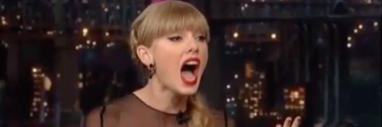 A screen shot of a GIF of Taylor Swift, reacting with hands in the air and her mouth open wide.