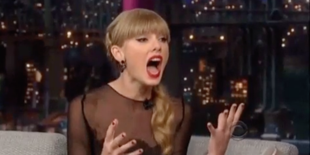 A screen shot of a GIF of Taylor Swift, reacting with hands in the air and her mouth open wide.