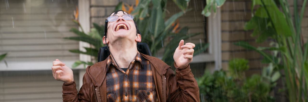 JJ looking up at the sky while it is pouring down and he is getting soaked, including his chair