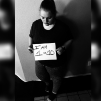 black and white photo of a woman holding a sheet of paper that says 'I am 1 in 10'