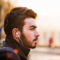 young bearded man against blurred background with earphones in his ears looking into distance