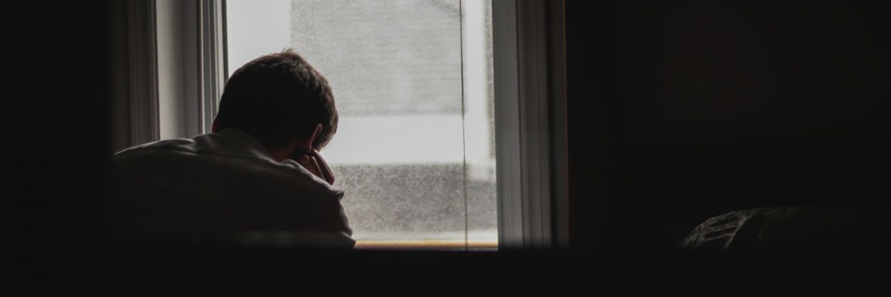 The Real Reason Asking for Help Is Hard When You Have Depression man looking out window in dark room alone depression