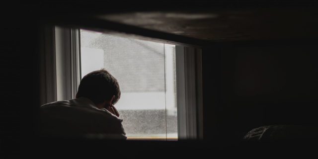 man looking out window in dark room alone depression