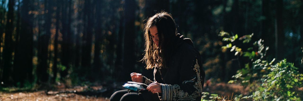 Your Story of Pain Is Not More or Less Important Than Anyone Else's girl in the woods looking at a notebook