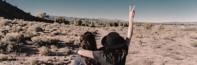 two women in the desert, one woman holding up the peace sign