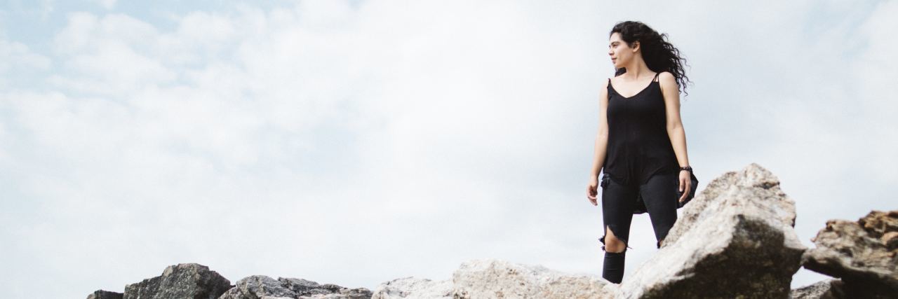 The Symptoms I Had That Were Signs of Hypermobility woman wearing black and standing on top of rocks looking off into the sky
