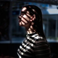 woman looking out window with shadow of blinds on her face