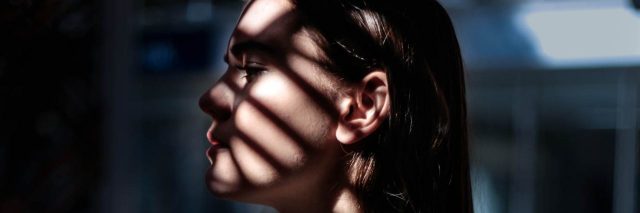 woman looking out window with shadow of blinds on her face