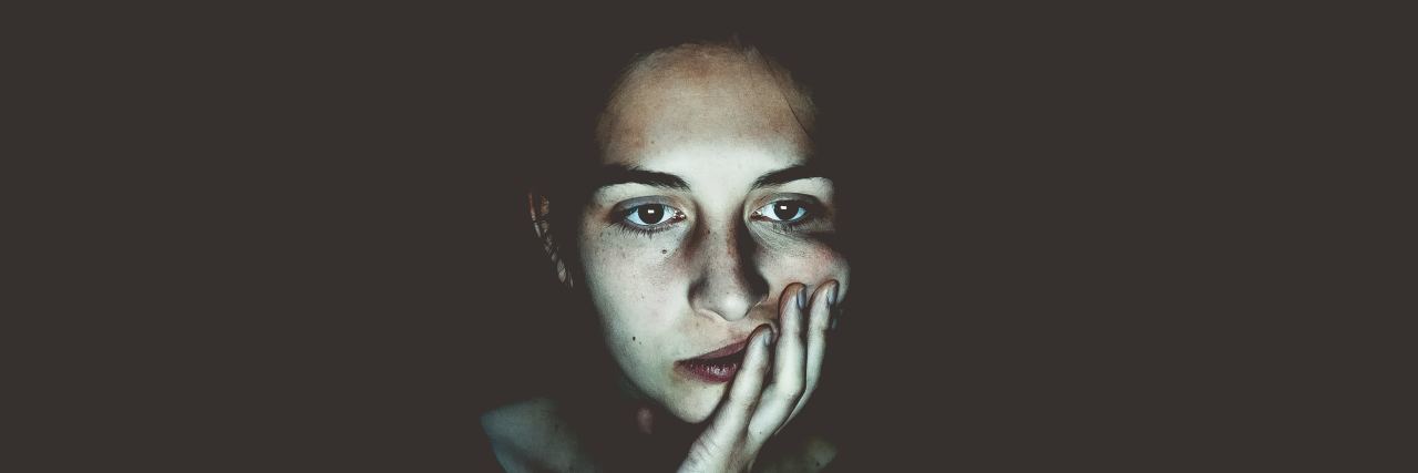 Answering 'How Are You' When My Body's in Pain and I'm Not Good woman in the dark looking like she's contemplating