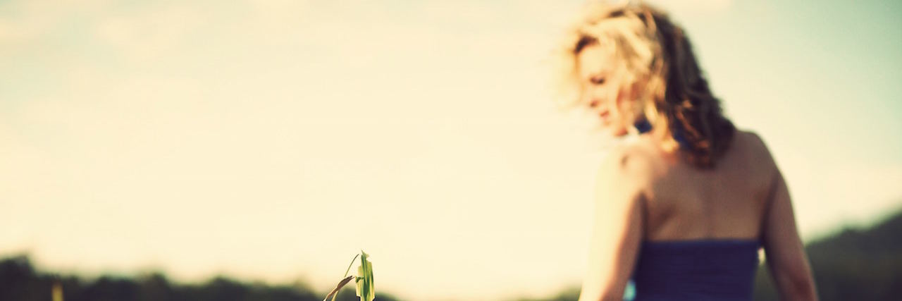 What It's Like Living With Both BPD and Bipolar Disorder A blurry portrait of a woman walking in a tall filed of grass, wearing a long dress.