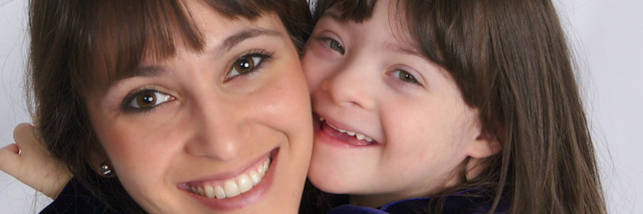 If You Don't Think You Want a Baby With Down Syndrome, Read This Mother hugging daughter with Down syndrome, face close up.