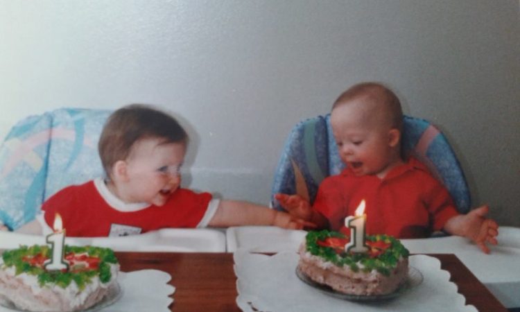 Twins celebrating their first birthday, they are reaching and touching each other. One baby has Down syndrome.